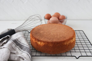 sponge cake on a cooling rack with whisk and eggs