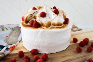 A Raspberry Cake with fluffy Vanilla Bean Meringue frosting garnished with raspberries