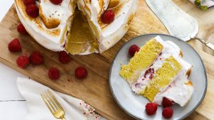 Beautiful Raspberry Cake topped with fluffy Vanilla Bean Meringue and fresh raspberries, with one slice on a plate