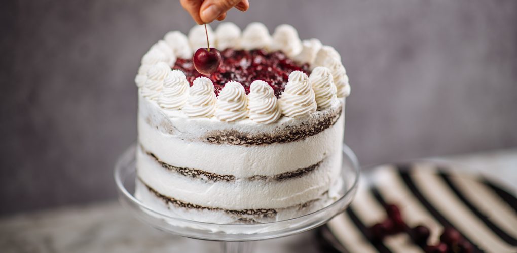 a whole black forest cake with white frosting and cherries on top