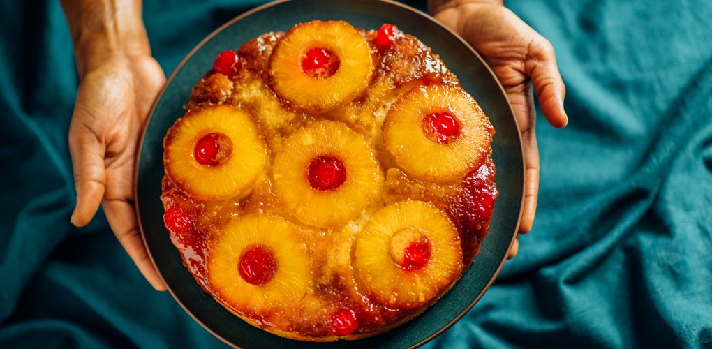 Hands holding a Pineapple Upside Down Cake on a serving plate