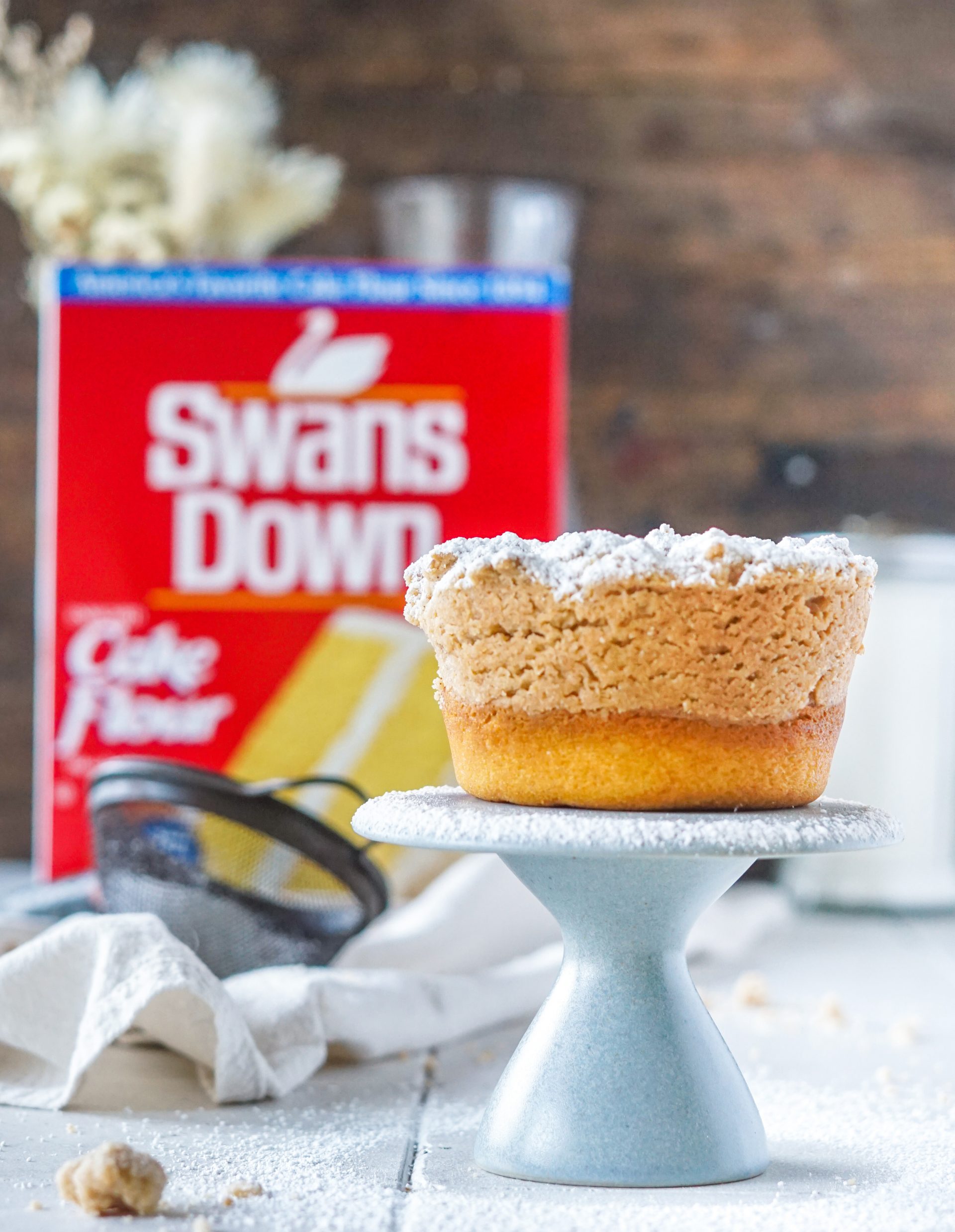 mini crumb bundt cake on a tiny pedestal with swans down box and sifter in background