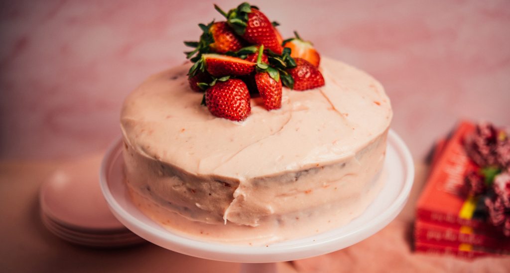 A whole Strawberry Preserves Cake with pink frosting and fresh strawberries on top