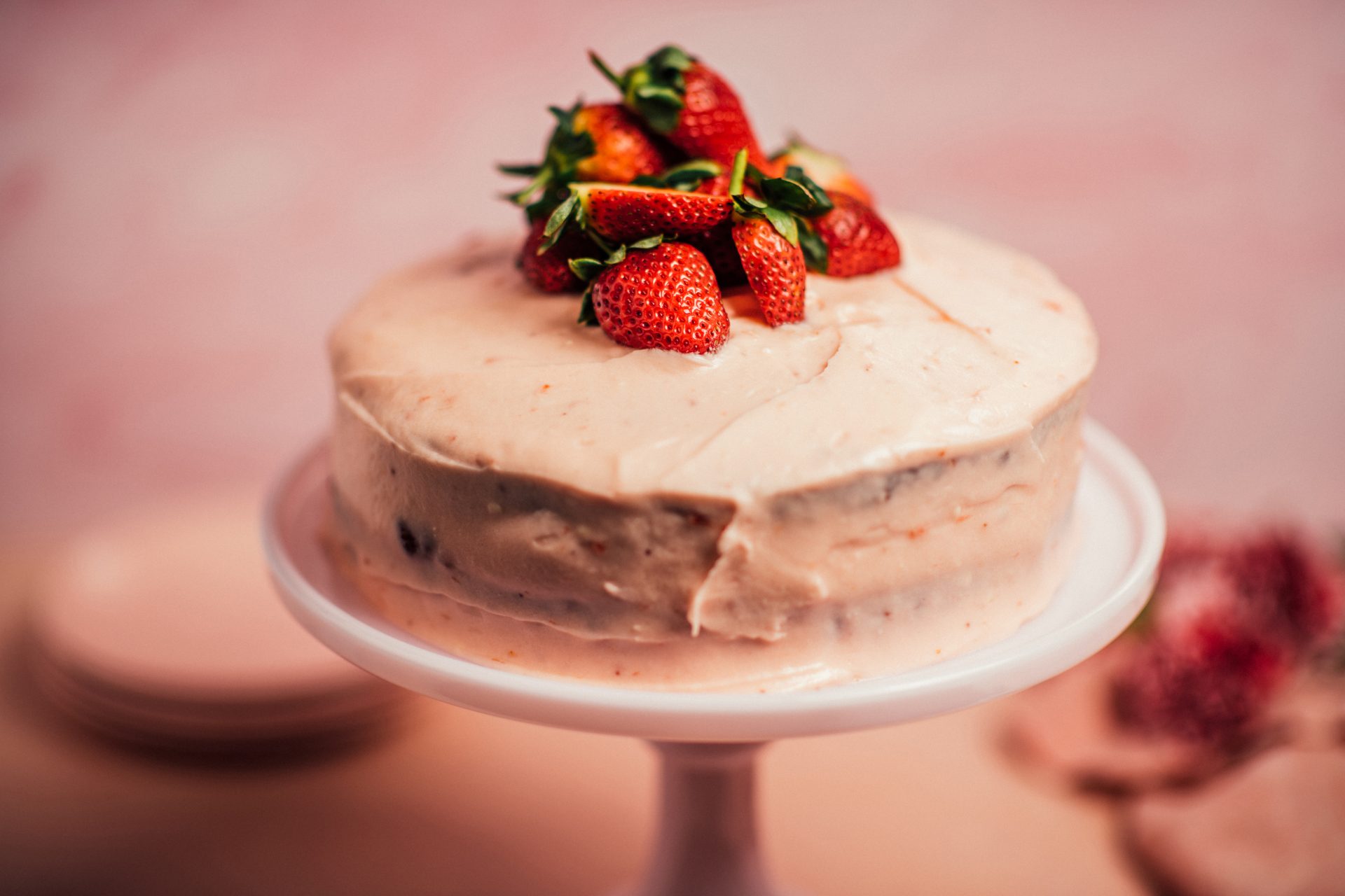 close up image of pink-frosted Strawberry Preserves Cake topped with fresh strawberries
