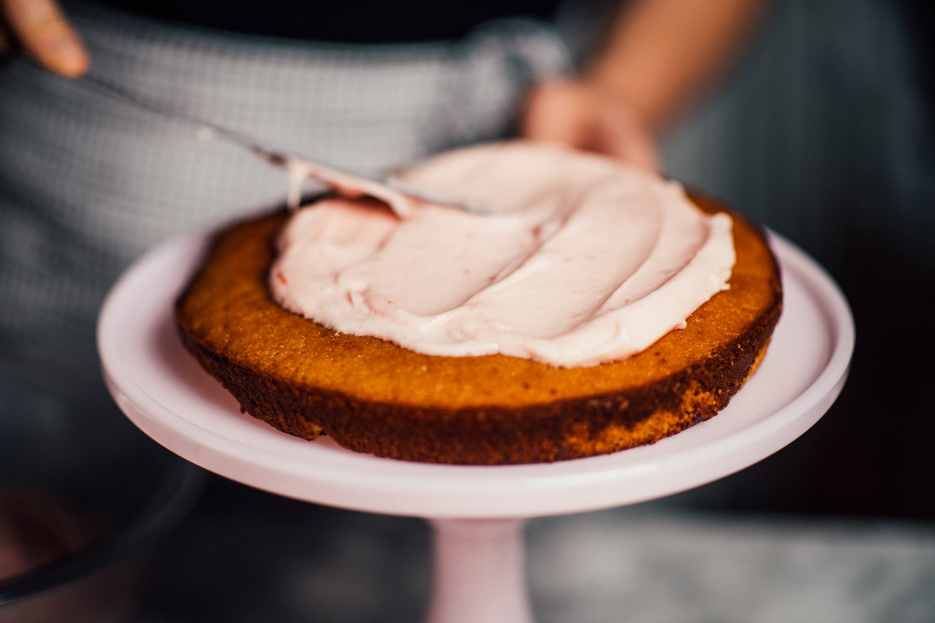 First cake layer of Strawberry Preserves cake laid on cake stand with filling frosting being applied