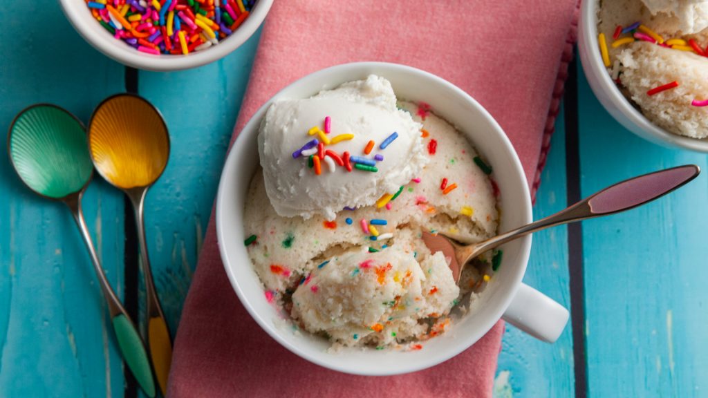 White Funfetti Cake topped with colorful sprinkles, in a mug