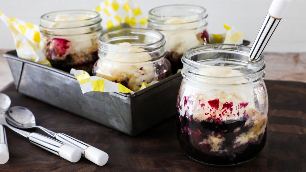 individual clear glass jars of blueberry dump cake on a serving tray with spoons